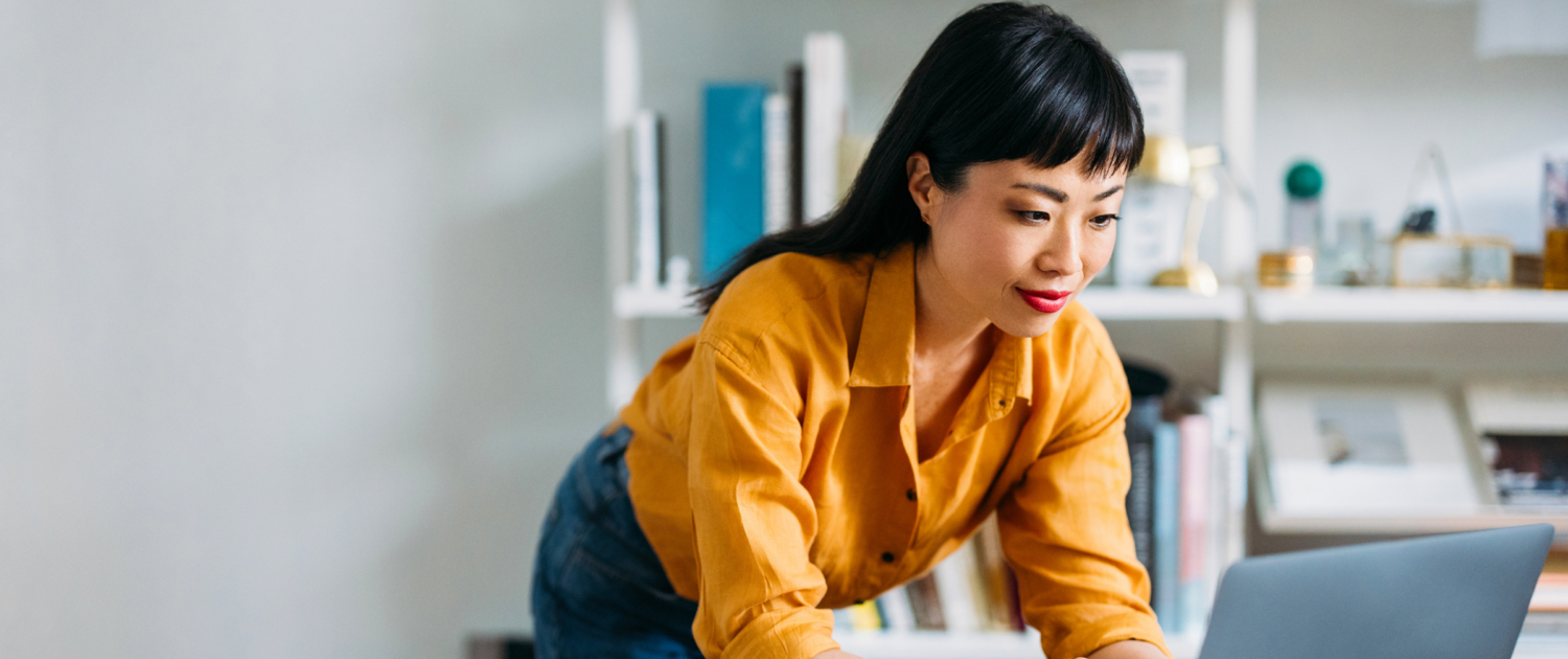 Woman standing in home office bent over looking at laptop computer