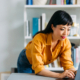 Woman standing in home office bent over looking at laptop computer