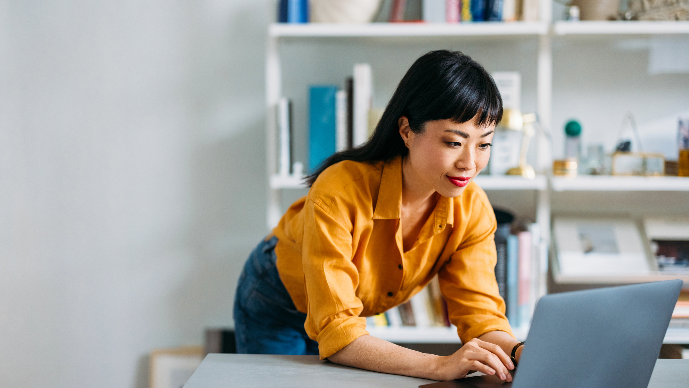 Woman standing in home office bent over looking at laptop computer