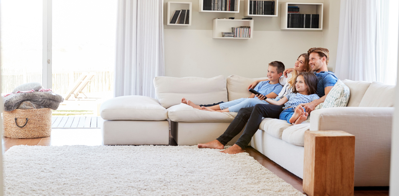 Family of our sitting on white couch watching TV in family room