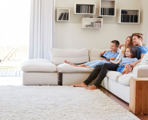 Family of our sitting on white couch watching TV in family room