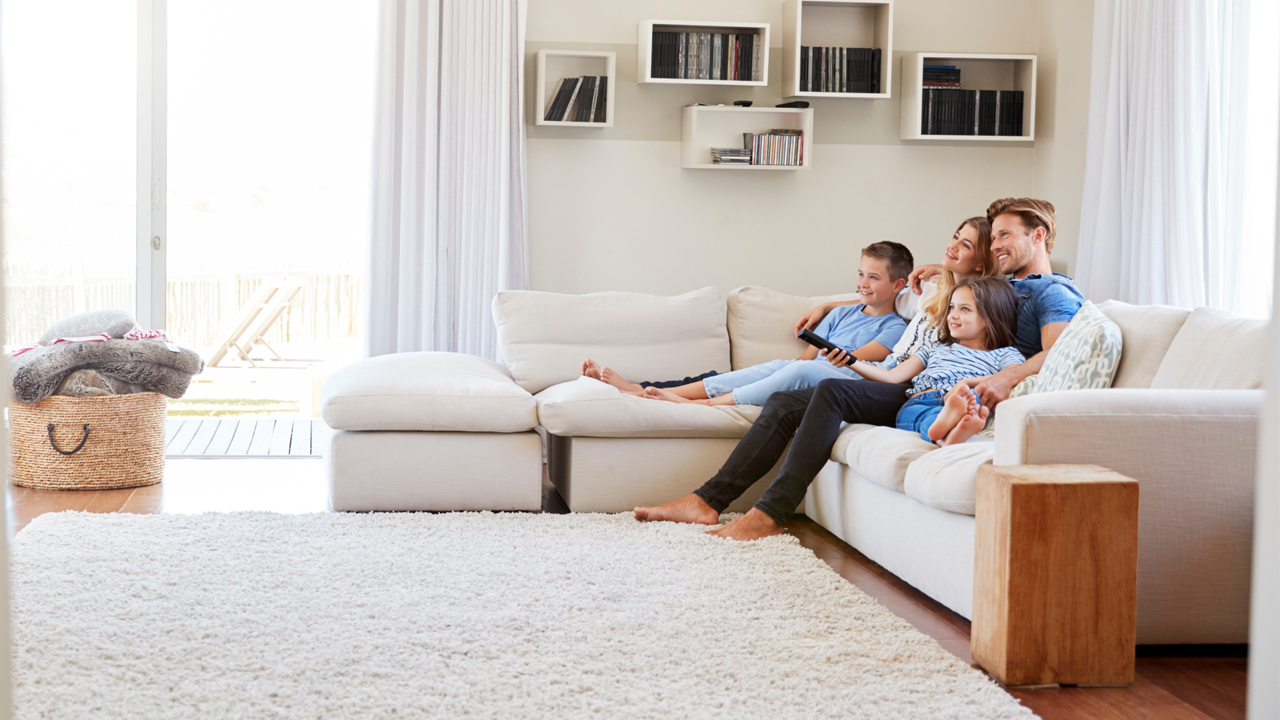 Family of our sitting on white couch watching TV in family room