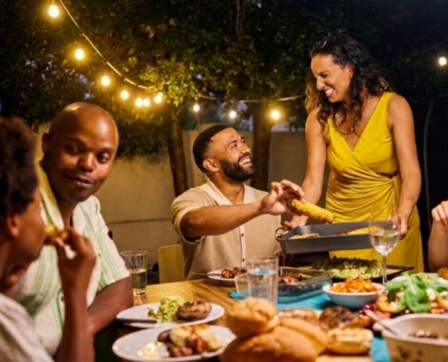 Family and friends share a laugh at an outdoor dinner table under string lights.