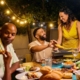 Family and friends share a laugh at an outdoor dinner table under string lights.