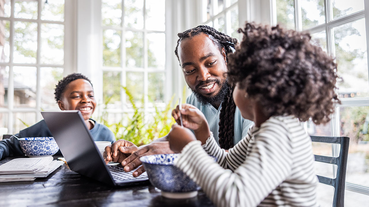 Father trying to work on laptop while his young children are distracting him